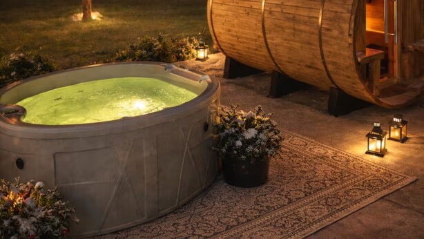 Una vasca idromassaggio e una struttura a botte di legno con una porta, circondata da un giardino con luci a stringa e piante in vaso.