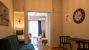 Een moderne woonkamer met een groene bank, een eettafel met stoelen en een wandklok.