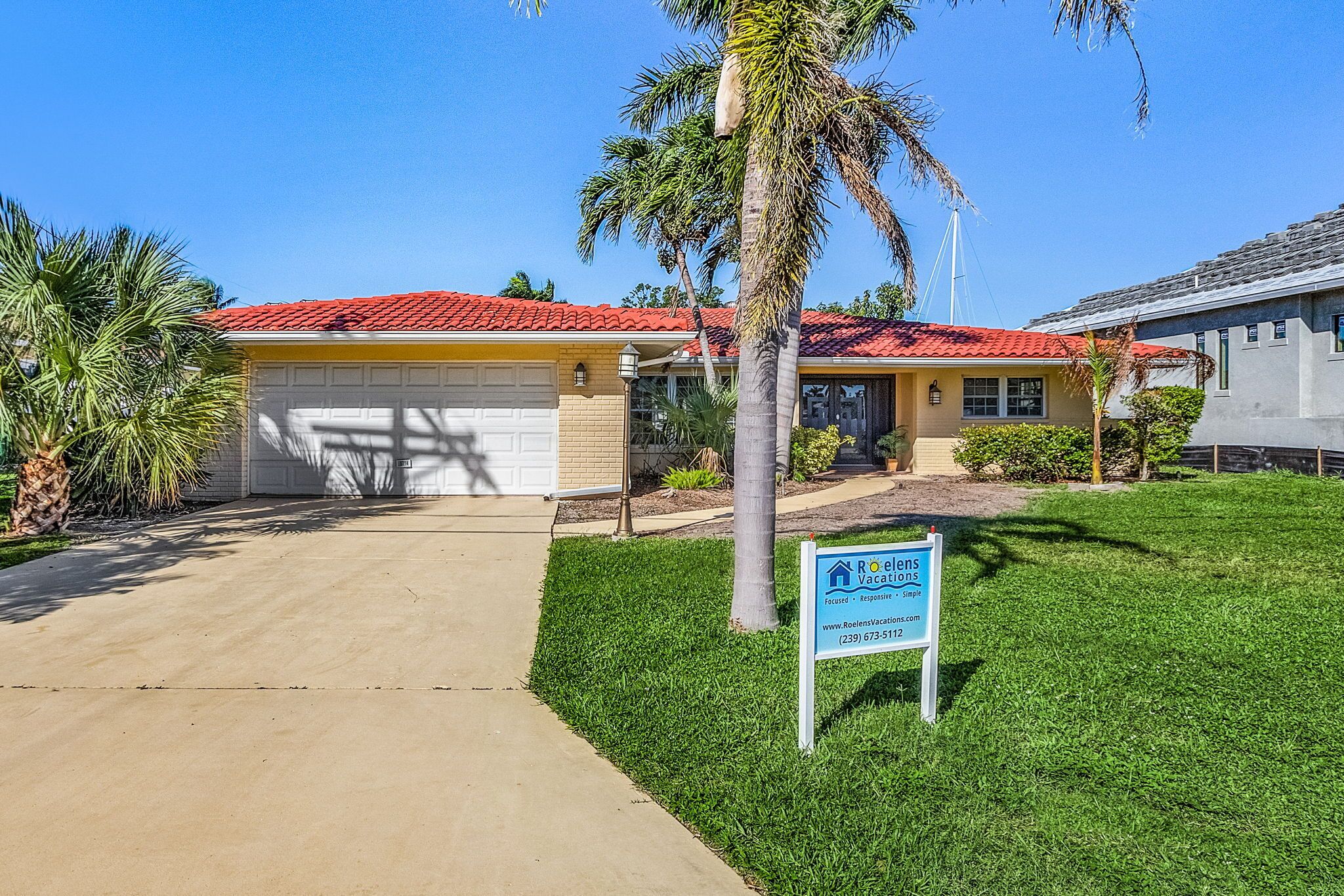 A residential house with a red-tiled roof, a garage, and a well-maintained lawn with palm trees.