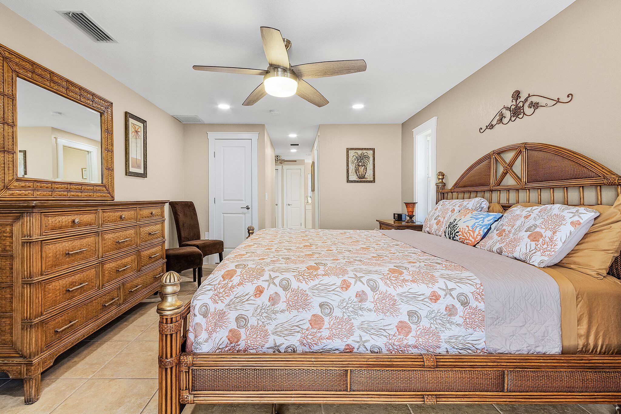 A bedroom with a bed, dresser, chair, ceiling fan, and wall decor.