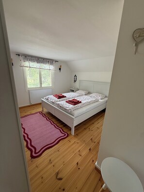 Una camera da letto con un letto, un comodino, una finestra con tende e un pavimento in legno.