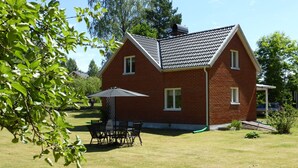 Een huis van baksteen met een schuin dak, een terras met tafel en stoelen, en een gazon.