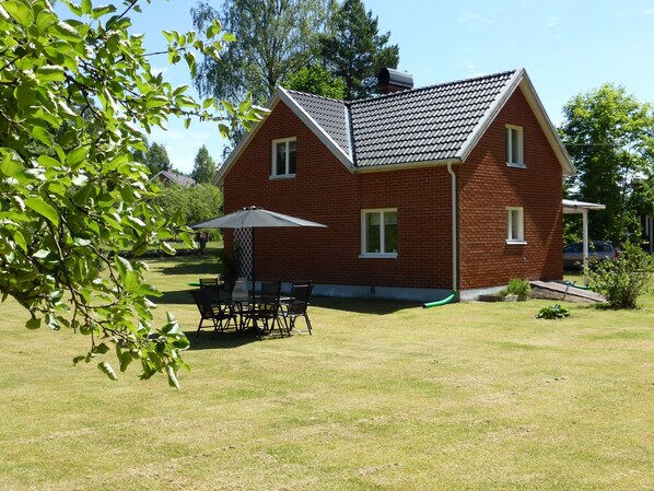 Une maison en briques avec un toit en pente, une terrasse avec une table et des chaises, et une pelouse.