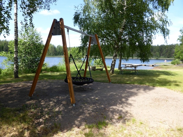Eine Schaukel mit Autoreifen, ein Picknicktisch und ein See im Hintergrund.