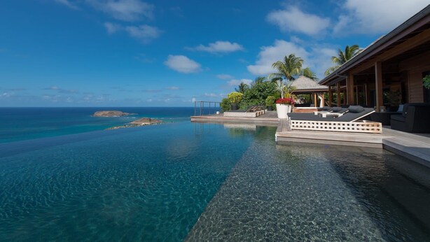 A infinity pool with clear blue water, a wooden deck, and a lounge area with cushions. - Villa Jade – Zen-Inspired Oceanview Estate with Spa, Cinema & Infinity Pool in St. Barths (Gustavia)