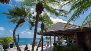 A wooden deck with a view of the ocean, palm trees, and a covered seating area with a Buddha statue. - Villa Jade – Zen-Inspired Oceanview Estate with Spa, Cinema & Infinity Pool in St. Barths (Gustavia)