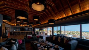 A spacious living area with a large sofa, a coffee table with magazines and candles, and a view of the ocean through large windows. - Villa Jade – Zen-Inspired Oceanview Estate with Spa, Cinema & Infinity Pool in St. Barths (Gustavia)