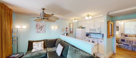 A compact living space with a kitchenette, a ceiling fan, and a sofa with patterned cushions.