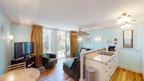 Ein modernes Wohnzimmer mit Fernseher, Sofa und Essbereich. Es verfügt über eine Küche mit Spüle sowie einen Balkon mit Vorhängen.
