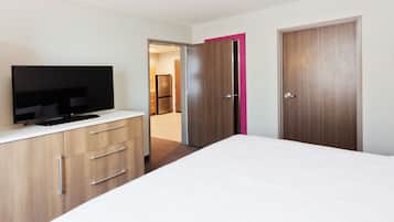 Ein modernes Schlafzimmer mit einem Flachbildfernseher auf einer Holzkommode, einem weißen Bett und zwei Türen, wobei eine Tür einen rosafarbenen Akzent aufweist.