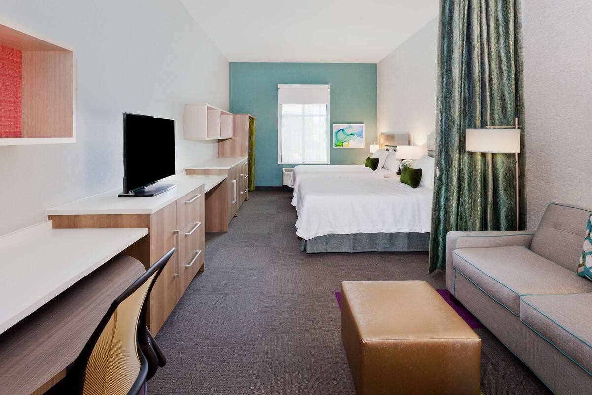 A hotel room with a bed, a sofa, a desk, a television, and a window with curtains.
