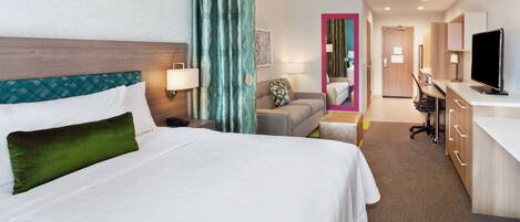 Habitación de hotel con una cama grande, un escritorio, una silla, un televisor y un baño visible a través de una puerta abierta.
