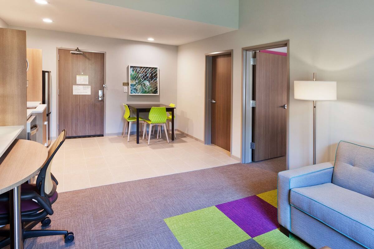 A hotel room with a desk, chairs, a sofa, and a colorful rug.