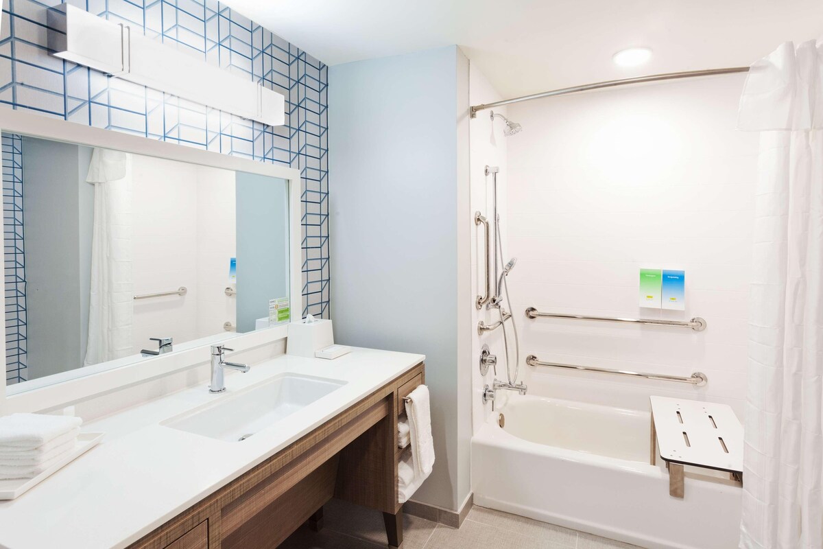 A modern bathroom with a large mirror, two sinks, a bathtub, and a shower.