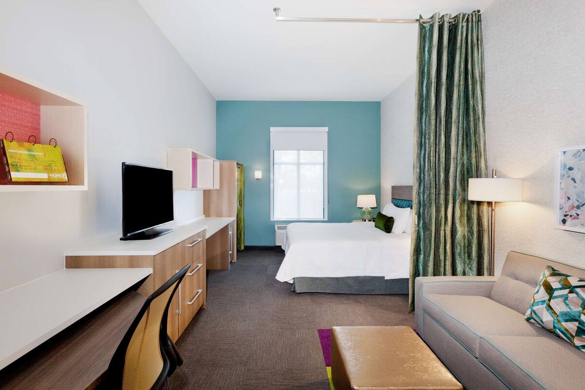 A hotel room with a bed, a desk, a chair, a sofa, and a television.