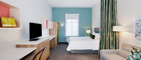 A hotel room with a bed, a desk, a chair, a sofa, and a television.