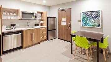 A modern kitchen with wooden cabinets, stainless steel appliances, and a dining area with bright green chairs.