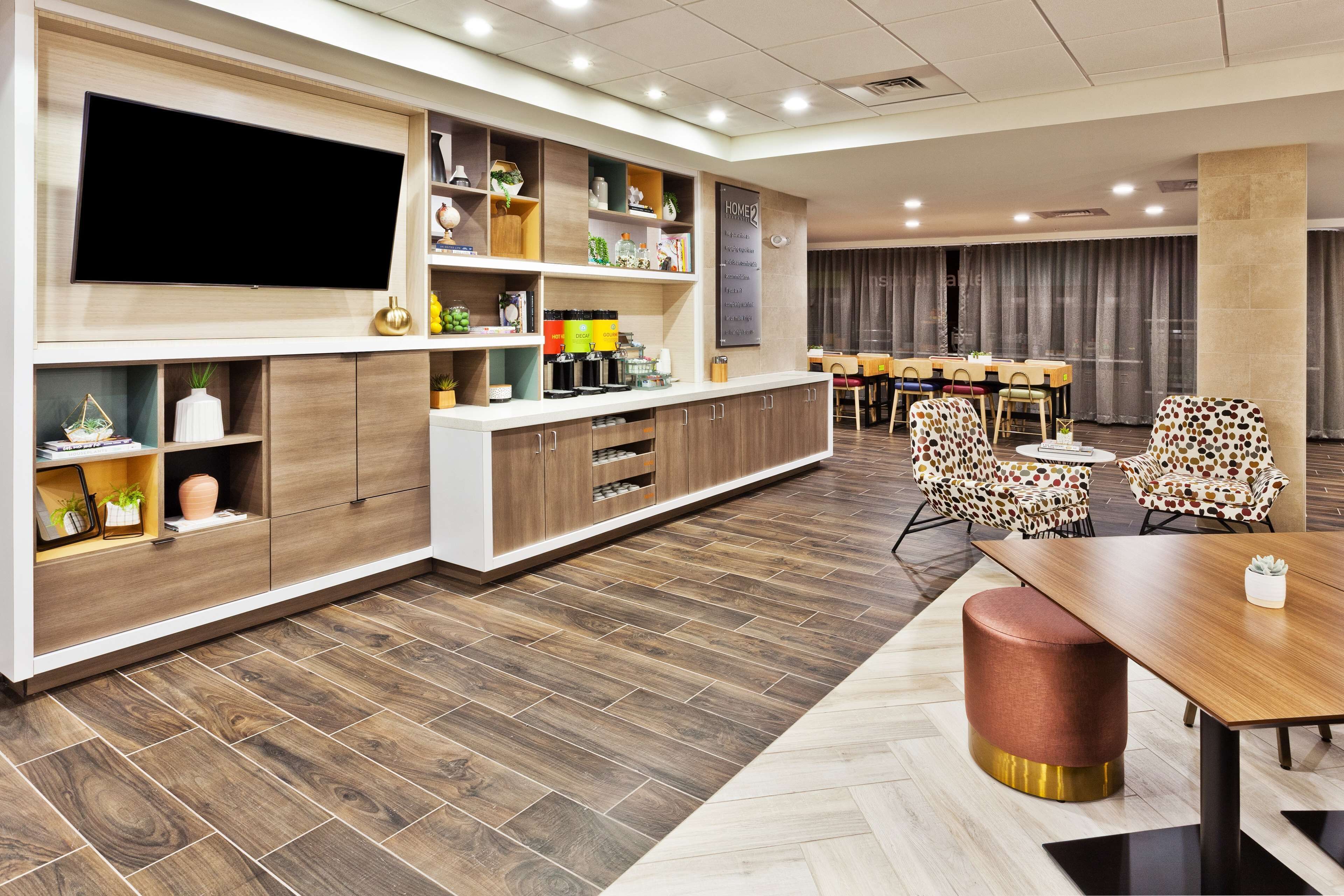 A modern conference room with a large flat-screen TV, wooden shelving with various items, a herringbone-patterned floor, and patterned chairs.