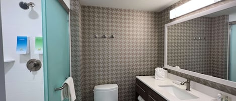 A bathroom with a toilet, sink, and shower. There are towels and toiletries on the counter.