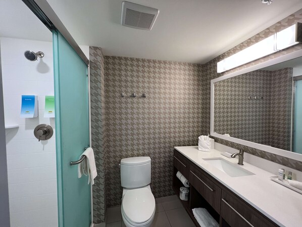 A bathroom with a toilet, sink, and shower. There are towels and toiletries on the counter.
