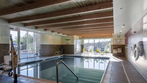 Una piscina interior con techo de madera, paredes de vidrio transparente y una silla para socorrista.