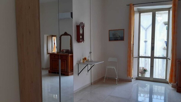 Una habitación con un armario de madera, un escritorio con silla, un espejo, un reloj y una ventana con cortinas.