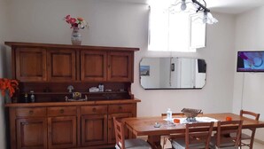 Un comedor con una mesa y sillas de madera, un mueble con utensilios de cocina, un espejo y un televisor en la pared.