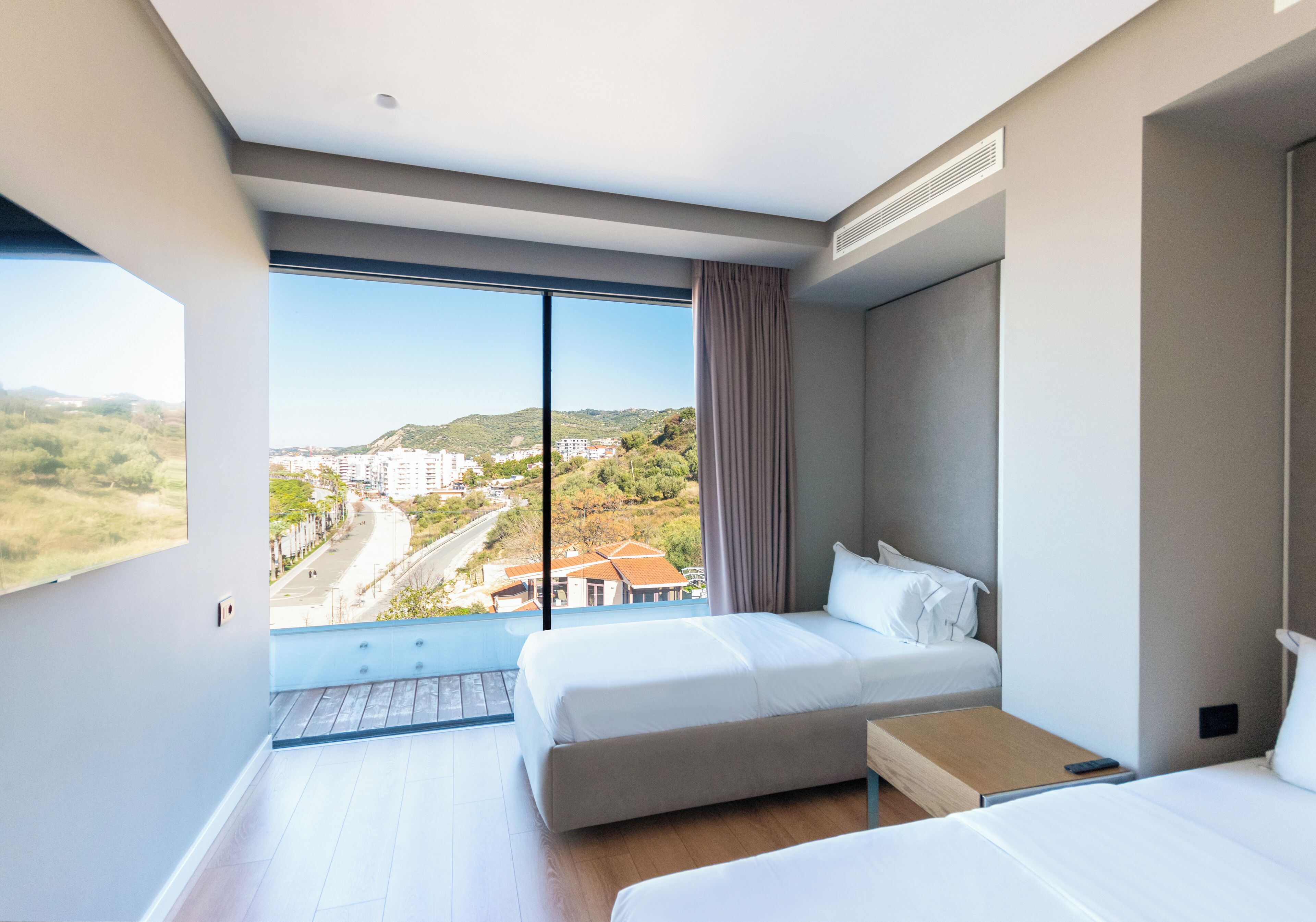 Una habitación de hotel moderna con dos camas, un ventanal amplio que ofrece vista a la ciudad y un balcón.