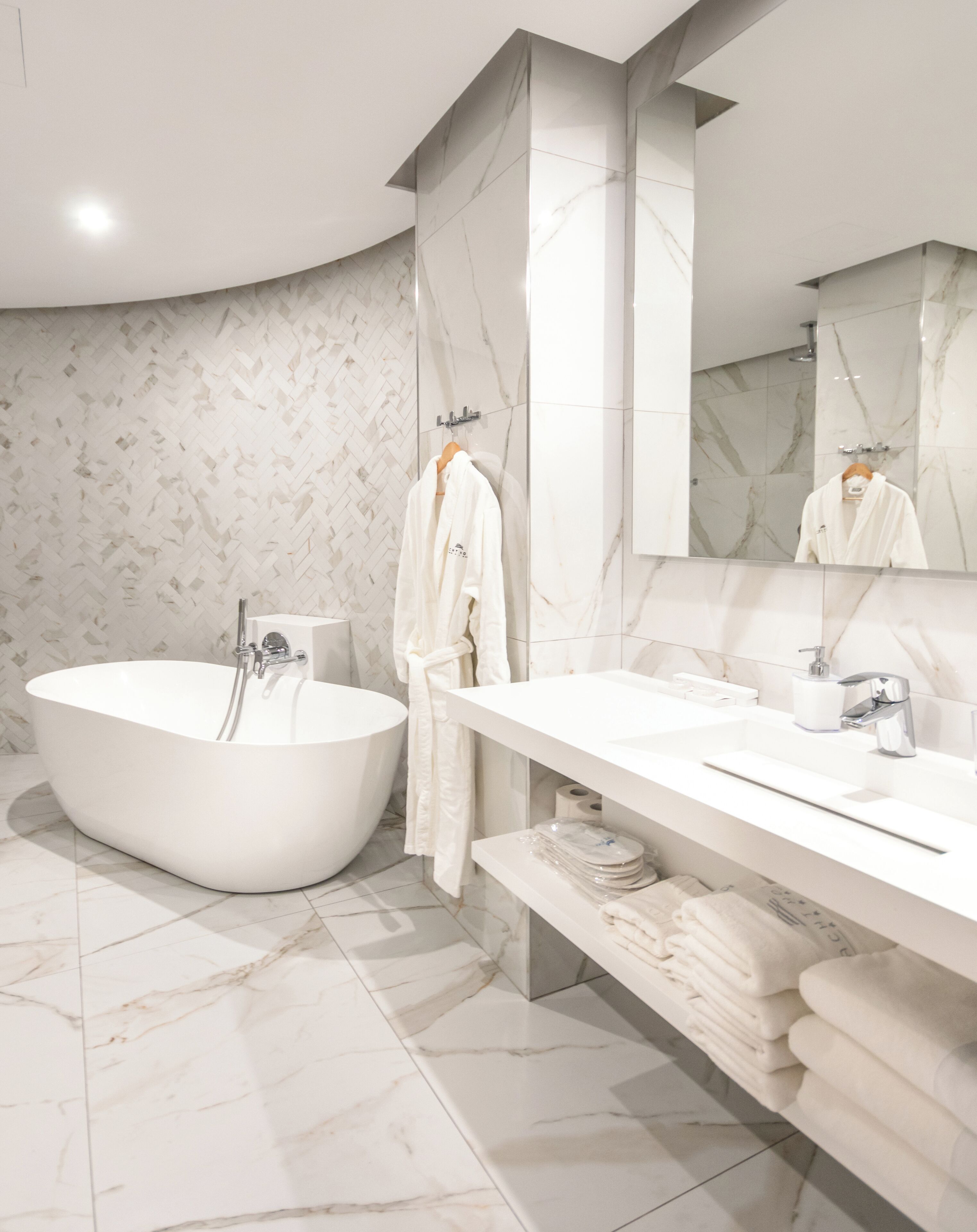 A modern bathroom with a freestanding bathtub, a vanity with a mirror, and marble flooring.
