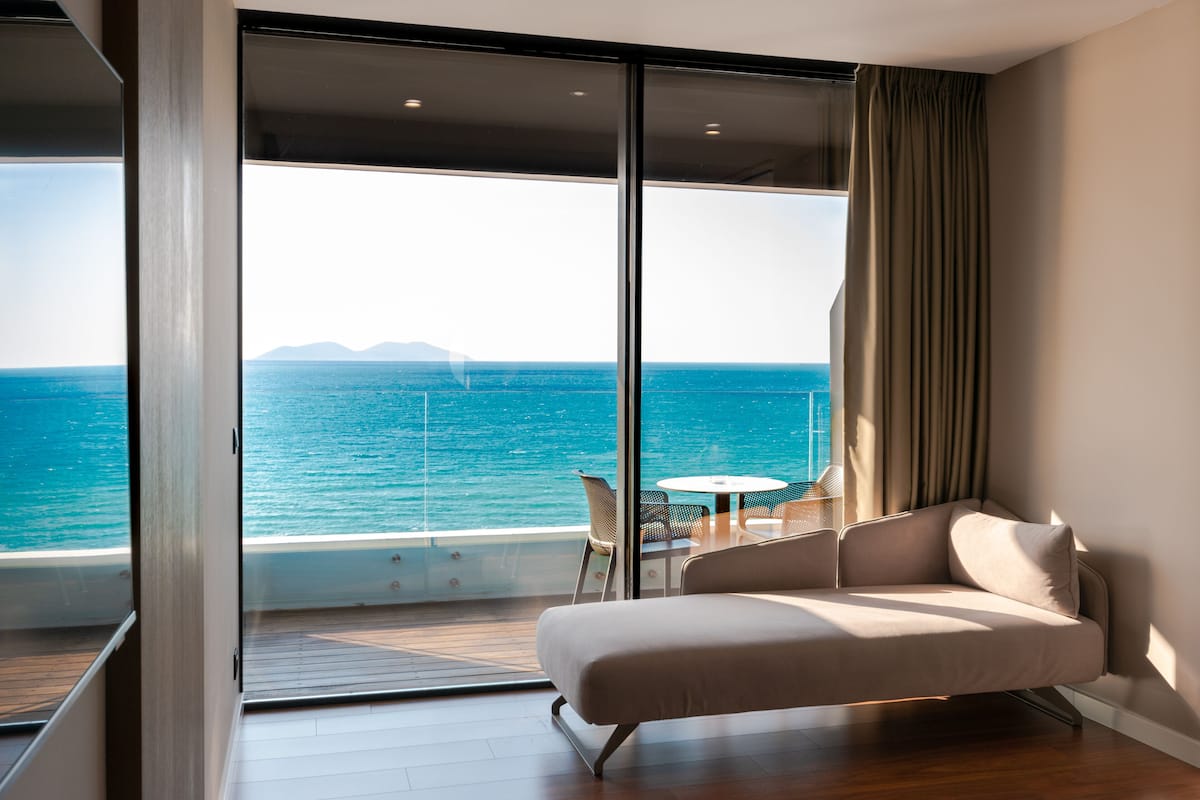 A modern room with a large sliding glass door leading to a balcony with a view of the sea.