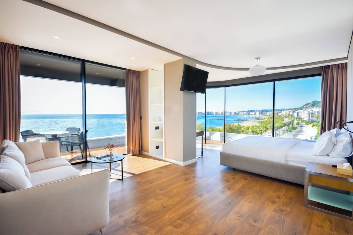 A modern hotel room with a large window offering a view of the sea and cityscape.