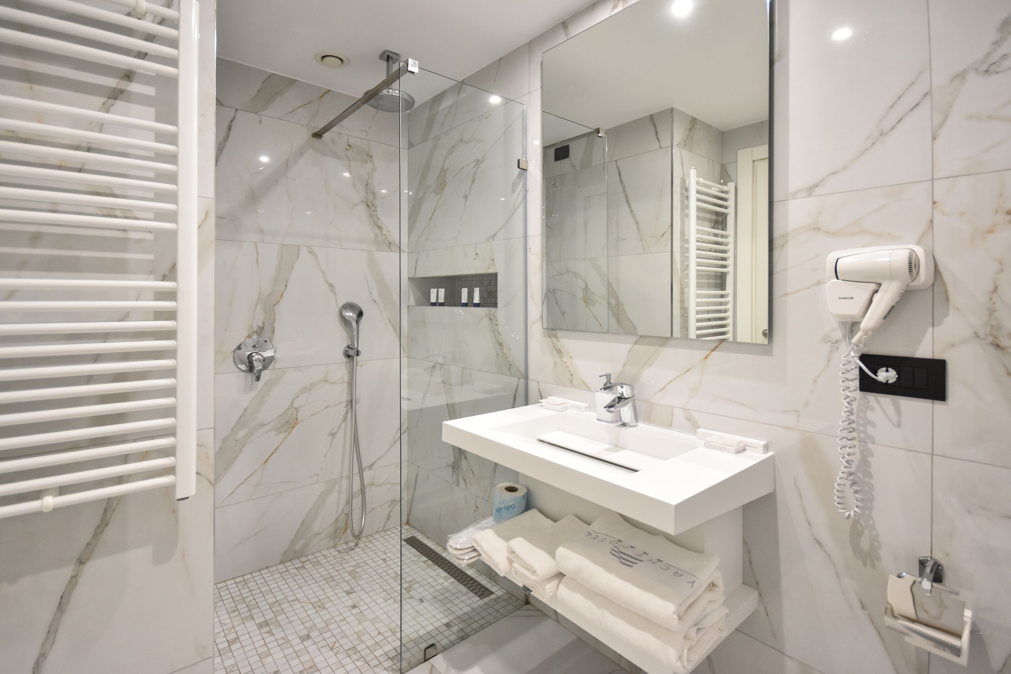 A modern bathroom with a glass-enclosed shower, a white vanity with a mirror, and a hairdryer mounted on the wall.