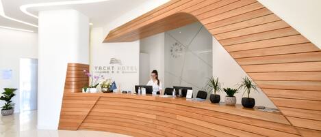 A reception desk with a wooden finish, a clock, and a sign that reads "Yacht Hotel".