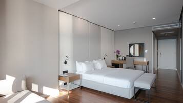 Ein modernes Hotelzimmer mit einem großen Bett, Nachttischen, einem Schreibtisch, einem Sessel, einem Spiegel und einem kleinen Badezimmerbereich.