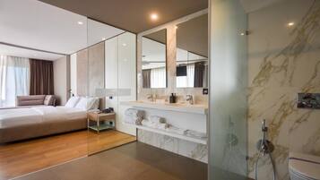 Una habitación de hotel moderna con una cama grande, cabina de ducha con mampara de vidrio y pared con azulejos de mármol.