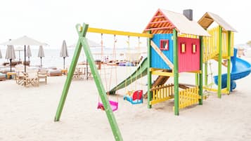 A beach playground with swings, slides, and a playhouse.