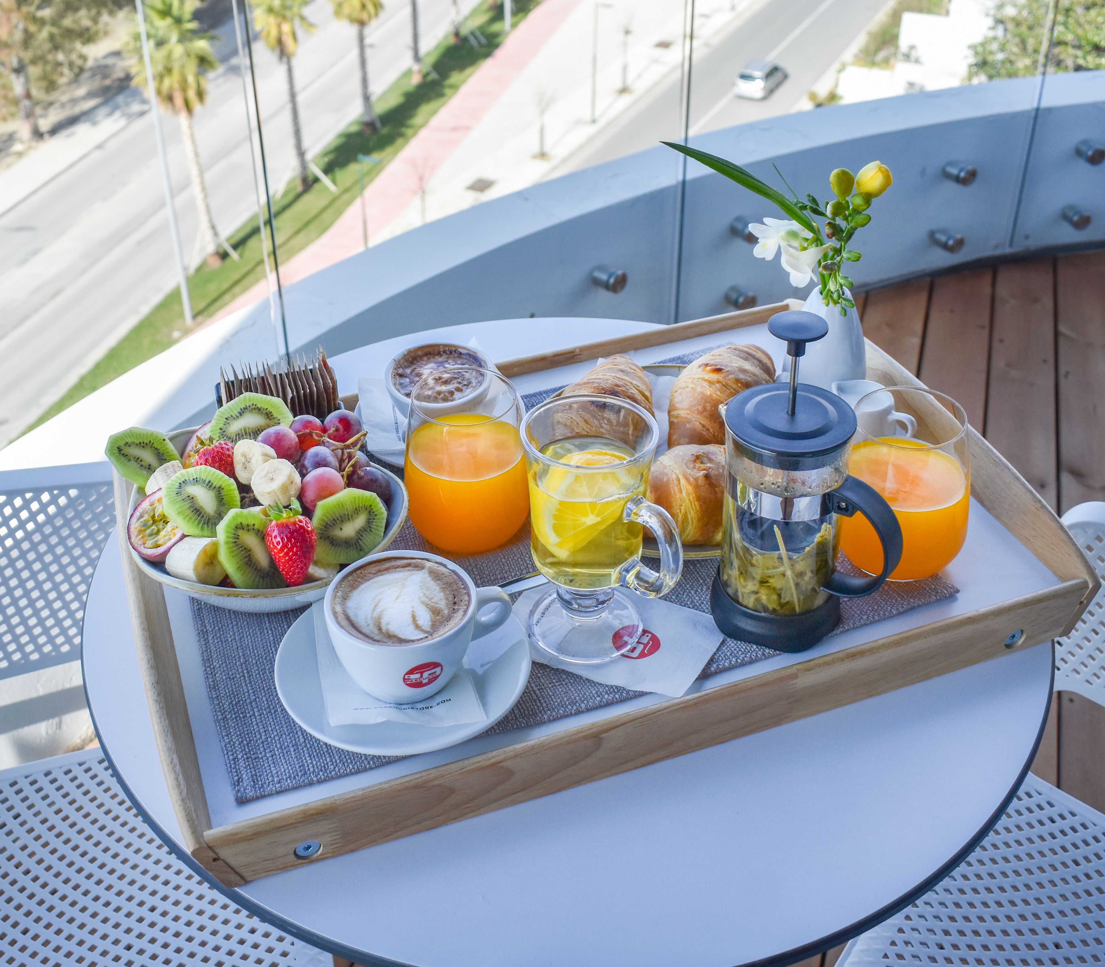 A breakfast tray on a balcony with fruits, pastries, coffee, and juice.