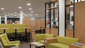 A modern lounge area with green upholstered seating, wooden tables, and a bookshelf with decorative items. - Super 8 by Wyndham Augsburg (Augsburg)