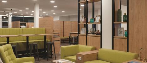 Un espace détente moderne avec des sièges verts, des tables en bois et une bibliothèque agrémentée d’objets décoratifs.