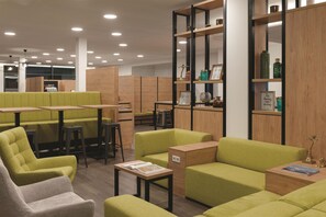 Ein moderner Lounge-Bereich mit grünen Sitzmöglichkeiten, Holztischen und einem Bücherregal mit Dekoration.