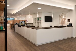 A modern reception area with a counter, shelves, and a mounted television.