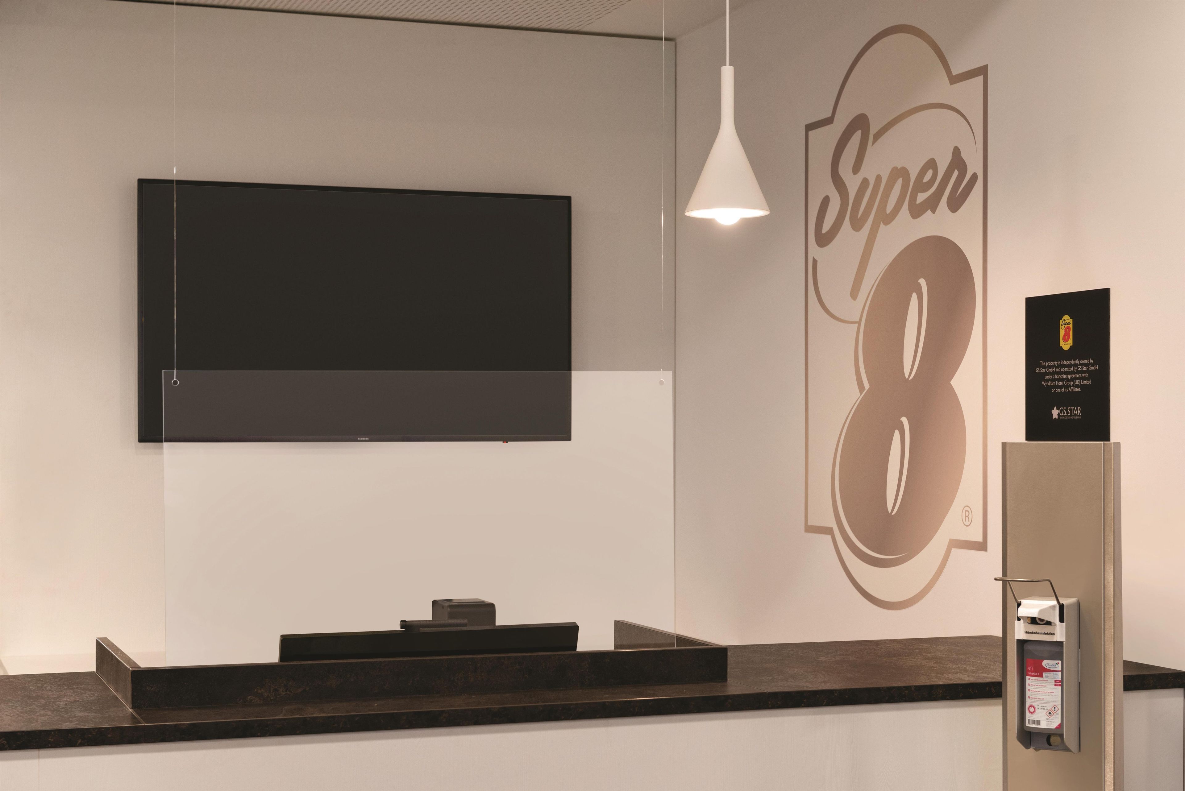 A reception desk with a flat-screen TV mounted above it, a wall-mounted sign with the number '8', and a hand sanitizer dispenser to the right.