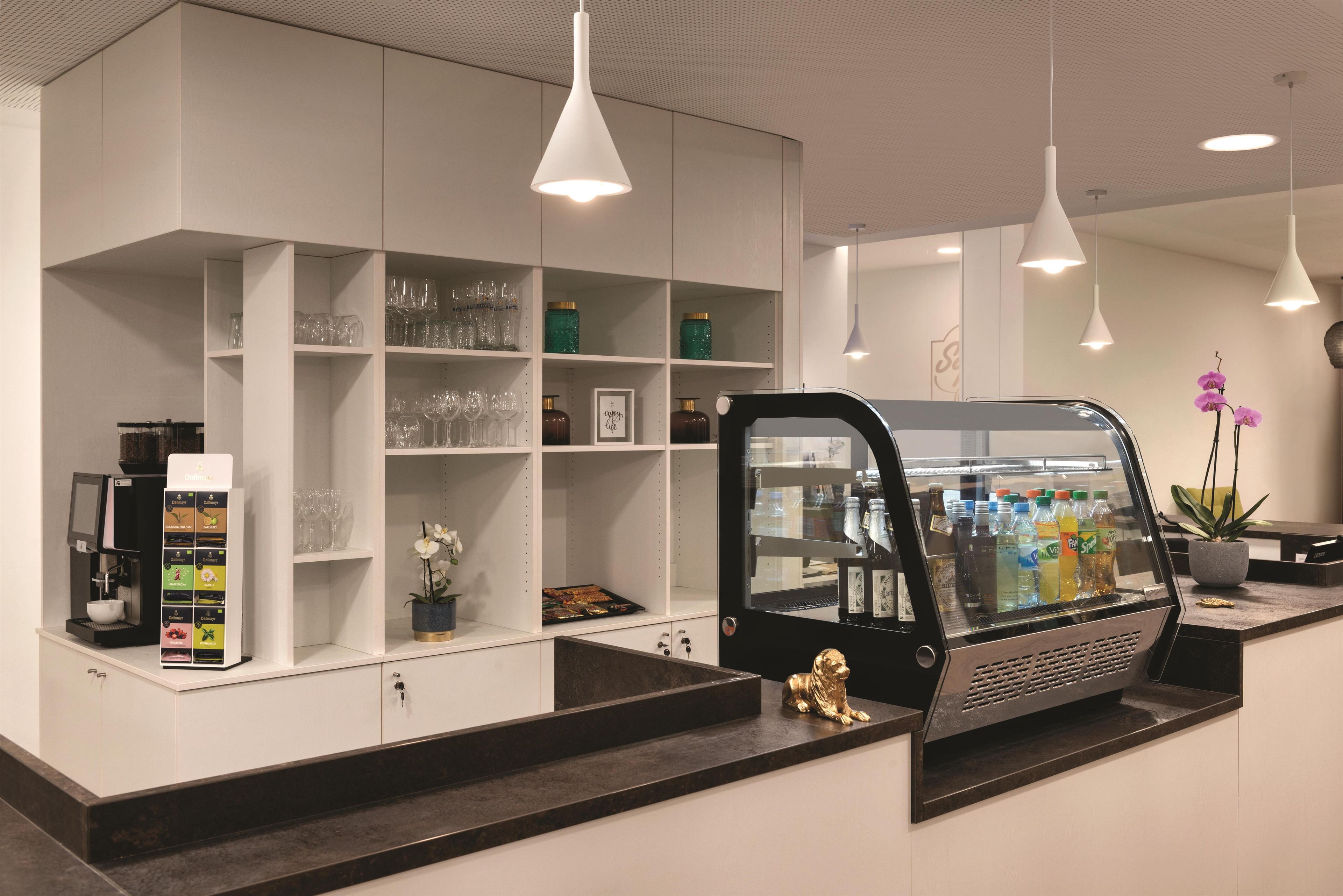 A modern reception area with a coffee machine, glassware, and a refrigerator stocked with beverages.