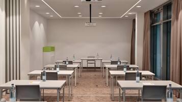 Una sala de conferencias con mesas, sillas, botellas de agua y un proyector en el techo.