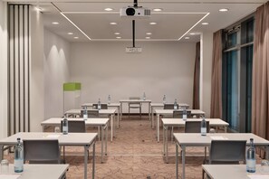 A conference room with tables, chairs, water bottles, and a projector on the ceiling.