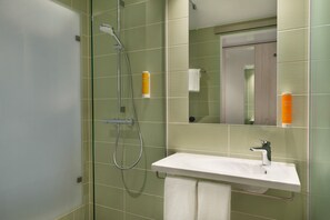 Een badkamer met een douchecabine van glas, een wit wastafelmeubel en een spiegel erboven.