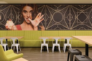 Ein Restaurantinneres mit grünen Sitzbänken, weißen Stühlen und einer Wand mit geometrischem Muster.