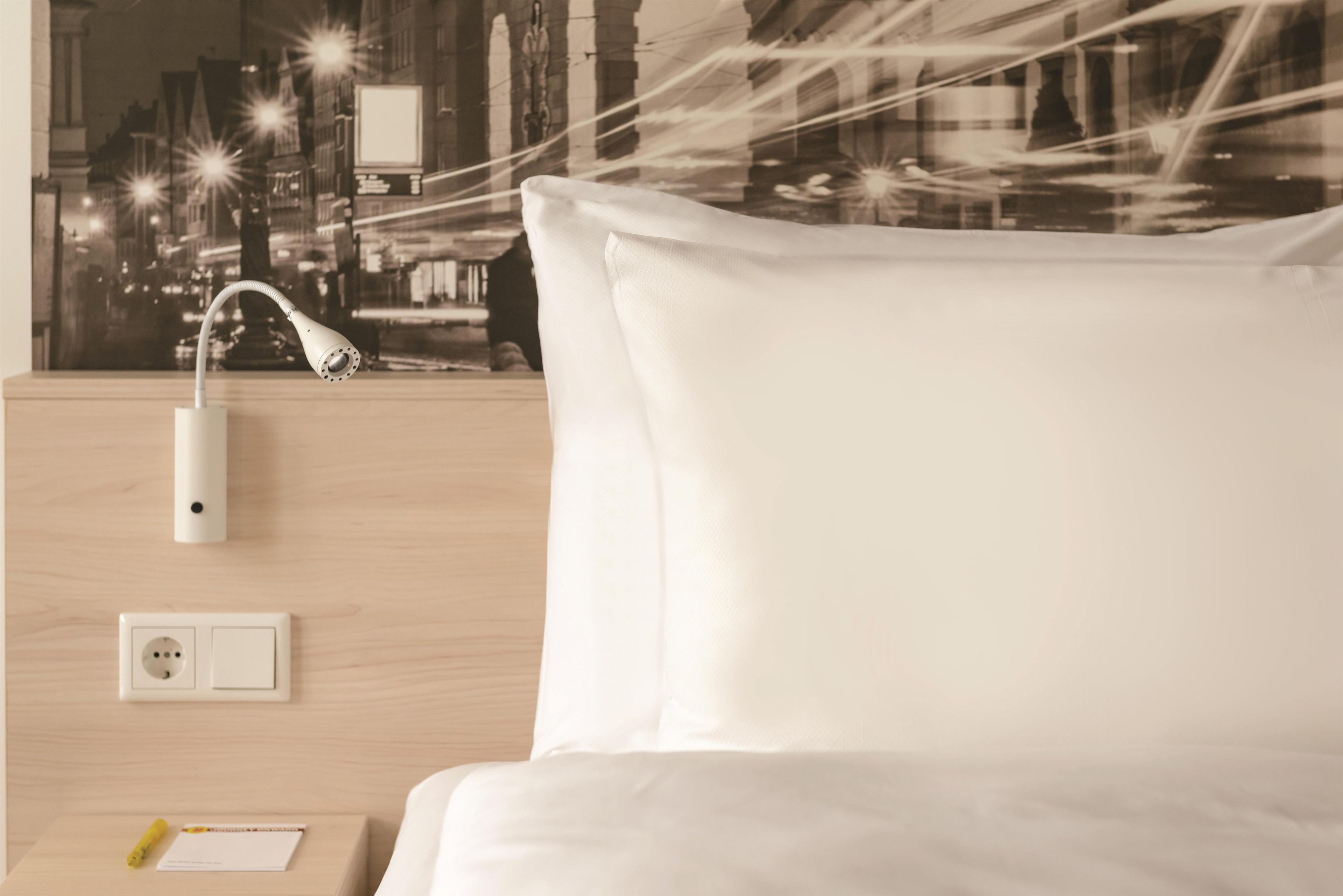 Habitación de hotel con cama, mesita de noche, toma de corriente y aplique de pared.