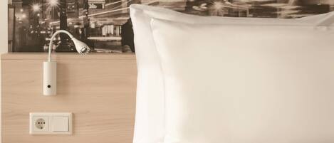 Habitación de hotel con cama, mesita de noche, toma de corriente y aplique de pared.