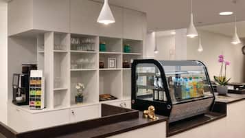 Un área de bar moderna con una máquina de café, estantes con vasos, un refrigerador con bebidas y una estatua de un león dorado.